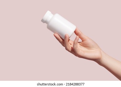 Female hand holding blank white squeeze bottle plastic tube on pink background. Packaging for pills, capsules or supplements. Mockup. High quality photo - Shutterstock ID 2184288377
