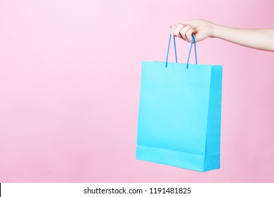 Female hand holding blue shopping bag on pink background - Powered by Shutterstock