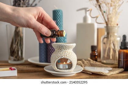 Female hand is holding a bottle of essential oil and dripping it in an aroma lamp for aromatherapy and calm relaxing atmosphere, concentration on meditation, care procedures and other rituals. - Shutterstock ID 2140352295