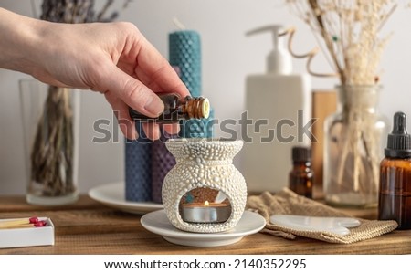 Female hand is holding a bottle of essential oil and dripping it in an aroma lamp for aromatherapy and calm relaxing atmosphere, concentration on meditation, care procedures and other rituals.