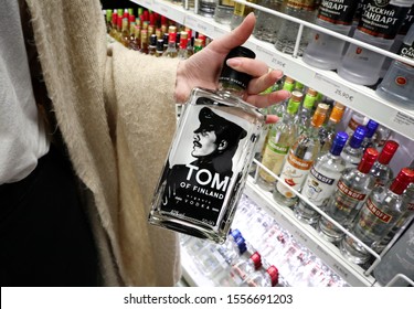 Female Hand Holding A Bottle Of Tom Of Finland Vodka. Various Brands Of Vodka In The Background. Tom Of Finland, Was A Finnish Artist Known For His Homoerotic Fetish Art. Helsinki, Finland -11-08-2019