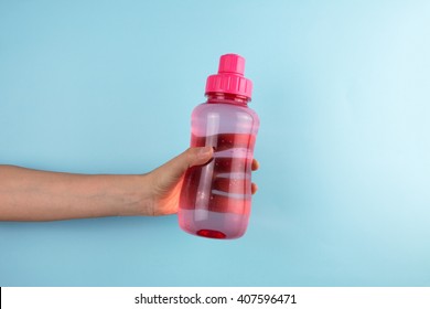 Female Hand Holding A Bottle Of Water On Blue Background.