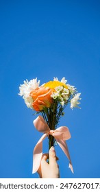 Female hand holding bouquet of flowers up to the sky, blue background, mother's day bouquet, bouquet of flowers