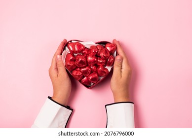 Female Hand Holding Box With Beautiful Red Chocolate Hearts Candies Pink Background Top View St Valentine Day Background