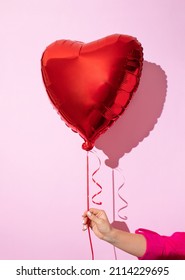 Female hand holding bright heart shaped red balloon. Festive background for Christmas, New Year, birthday concept, Valentine's day.