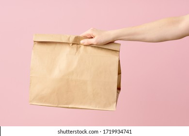 Female Hand Holding Brown Clear Empty Blank Paper Bag For Food Delivery On Pink Background With Copy Space. Packaging Template Mock Up Fast Food. 