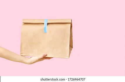 Female Hand Holding Brown Clear Empty Blank Paper Bag For Food Delivery On Pink Background With Copy Space. Packaging Template Mock Up Fast Food. 