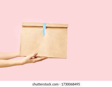 Female Hand Holding Brown Clear Empty Blank Paper Bag For Food Delivery On Pink Background With Copy Space. Packaging Template Mock Up Fast Food. 