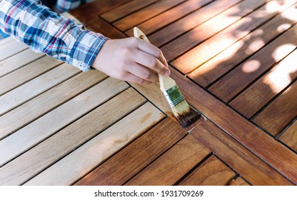 Female Hand Holding A Brush Applying Varnish Paint On A Wooden Garden Table - Painting And Caring For Wood With Oil