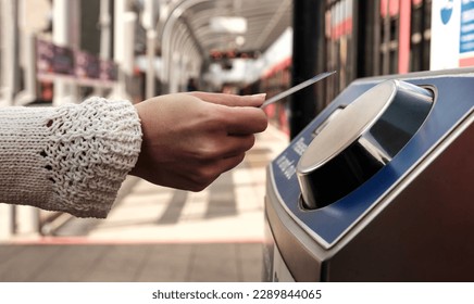 Female hand holding a card on contactless card reader machine in train station in London. There a blurry red train in the station. No cash public transport concept.