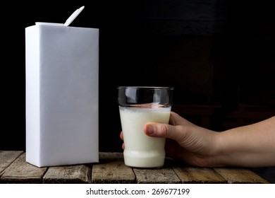 Female Hand Holding A Carton Of Milk And Pour Into A Glass On A Wooden Vintage Background