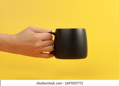 Female hand holding a coffee mug isolated on yellow background - Powered by Shutterstock