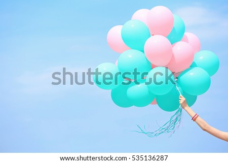 Female hand holding colorful balloons against blue sky