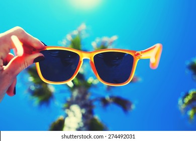 Female hand holding colorful sunglasses against palm tree and blue sunny sky, summer vacation holidays concept, first person shot, looking though glasses, filtered image - Powered by Shutterstock