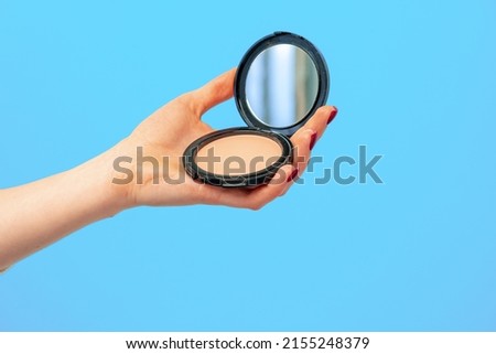 Female hand holding compact powder against blue background