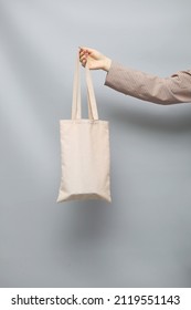 Female Hand Holding Cotton Shopper Minimalistic Shot On Grey Background With Space For Logo Or Design. Mock Up.