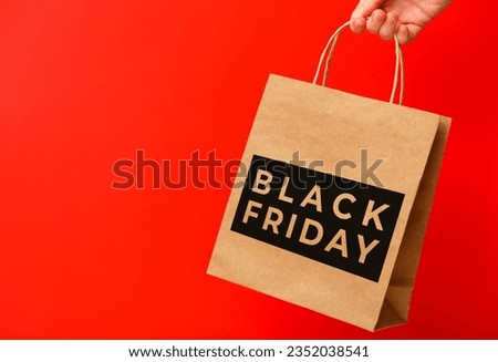 Female hand holding craft shopping bag with Black Friday text on red background. Sale, discount, shopping concept