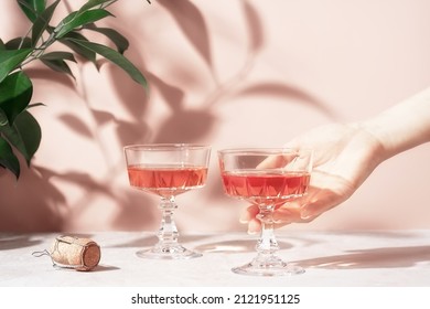 Female hand holding crystal glass of rose sparkling wine or champagne over pastel pink marble table in sunlight. Minimal creative composition with copy space. Summer drink concept.