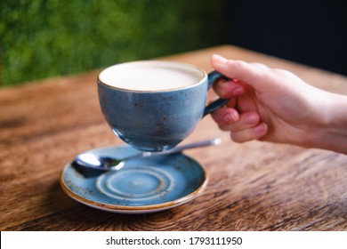 Female Hand Holding A Cup Of Cappuccino Coffee With Milk Foam In A Summer Cafe, Close Up