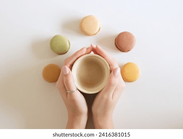 The female hand is holding a cup of coffee with macarons. White backgrounds. Flat lay, top view.  - Powered by Shutterstock