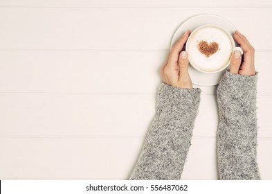 Female Hand Holding Cup Of Coffee On White Wooden Table. Photograph Taken From Above, Top View With Copy Space