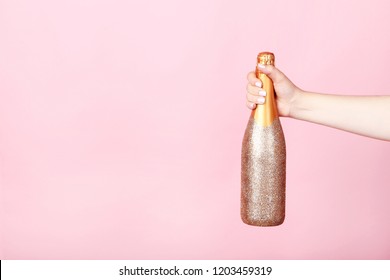 Female hand holding decorated champagne bottle on pink background