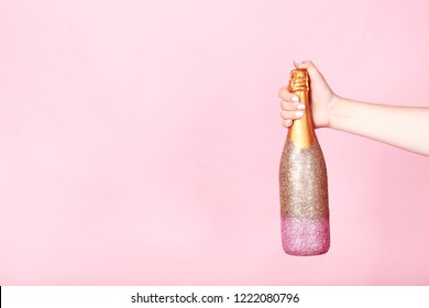 Female Hand Holding Decorated Champagne Bottle On Pink Background