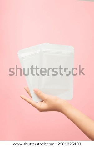 Female hand holding facial sheets mask white blank realistic mockup on trendy pink background. Mockup for package design, skincare, cosmetic beauty product for face.