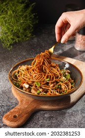Female hand holding a fork with Italian pasta spaghetti with chicken, green beans, cheese mozzarella and fresh thyme in green bowl on wooden board on grey concrete surface