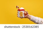 Female hand holding funny but cozy cup of Irish Coffee topped with whipped cream against warm yellow studio background. Concept of festive winter drink, cafe and catering, Christmas mood. Ad