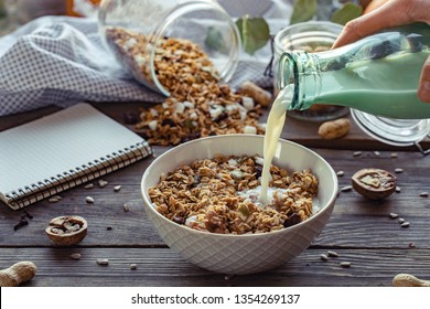 Female hand holding glass bottle pouring milk in cereal granola flakes bowl with nuts seeds raisins on brown wooden table background, healthy breakfast lifestyle concept, home muesli food oat meal - Powered by Shutterstock