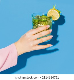 Female hand holding glass with cocktail mojito with lemon isolated on light blue neon background. Complementary colors, blue, yellow and green. Copy space for ad, text, design - Powered by Shutterstock