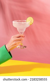 Mano femenina sosteniendo un vaso de delicioso cóctel de margarita aislado sobre fondo amarillo rosa. Saludos. Concepto de cócteles, bebidas alcohólicas, gusto, fiesta, mezcla. Copiar espacio para el anuncio. Estilo retro