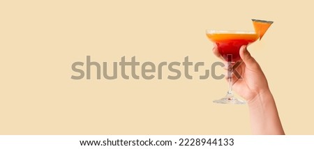 Female hand holding glass of tasty pumpkin pie martini on beige background with space for text