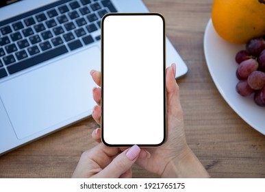 female hand holding golden phone with isolated screen on wooden table in office 