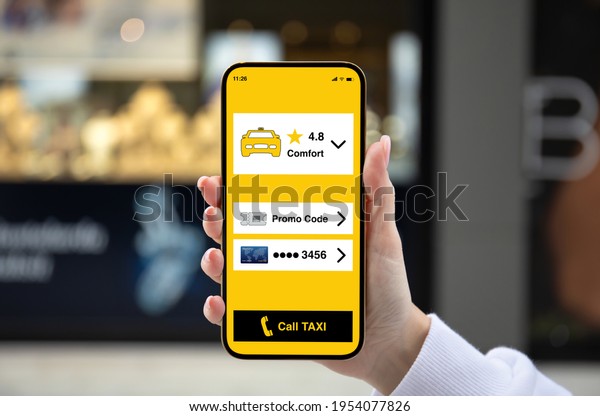 female hand holding golden phone with\
taxi call application on screen street background\
