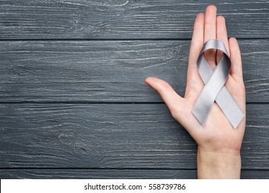 Female hand holding grey ribbon on wooden background. Brain cancer, diabetes, asthma concept
