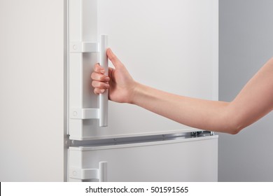Female hand holding handle of white refrigerator door on gray background