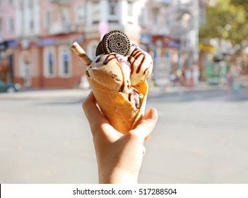 Female hand holding ice cream with chocolate sauce and cookies