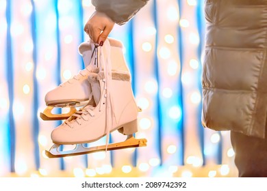 Female Hand Holding Ice Skates Against Lights Background In Winter.