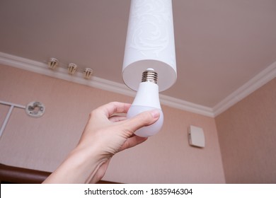 Female Hand Holding A Led Light Bulb To Change, Replace It At Home, Screwing In The Bulb Into A Lamp Holder For Energy Saving And Economy, Saving Money.