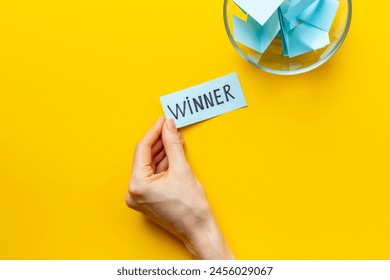 Female hand holding lottery ticket with winner word near glass bowl full of paper sheets. Winner concept. - Powered by Shutterstock