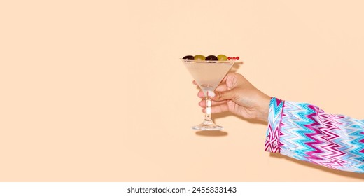 Female hand holding martini glass with a green olive on a stick against light background. Concept of alcohol and non-alcohol drink, party, holidays, bar, mix. Poster. Copy space for ad - Powered by Shutterstock