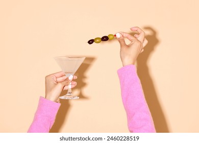 Female hand holding martini glass with a green olive on a stick against light background. Concept of alcohol and non-alcohol drink, party, holidays, bar, mix. Poster. Copy space for ad - Powered by Shutterstock