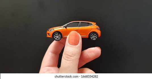 female hand holding metal car toy exact model of orange color on black background