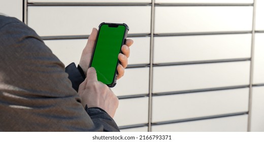 Female Hand Holding Mobile Phone With Green Screen Chroma Key Next To Parcel Locker Collecting Parcel From Shopping Locker. Woman Skans QR Code On Mobile Phone Self-service Locker Cell With Bar Code