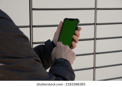 Female Hand Holding Mobile Phone With Green Screen Chroma Key Next To Parcel Locker Collecting Parcel From Shopping Locker. Woman Skans QR Code On Mobile Phone Self-service Locker Cell With Bar Code