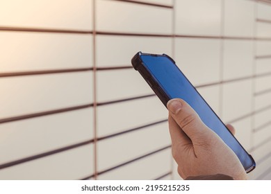 Female Hand Holding Mobile Phone Next To Parcel Locker Collecting Parcel From Shopping Locker. Woman Skans QR Code On Mobile Phone Self-service Locker Cell With Bar Code Reader Modern Shipping And