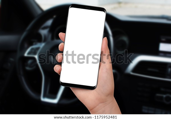 Female hand holding modern phone with\
isolated screen, steering wheel in background.\
Mockup