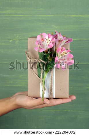 Female hand holding natural style handcrafted gift box with fresh flowers and rustic twine, on wooden background